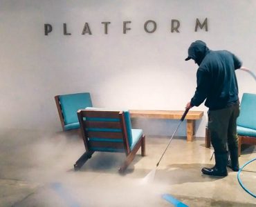 Crown Facility Solutions worker pressure washing concrete floors in common area