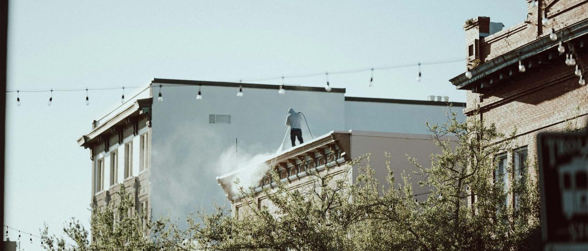Person pressure washing the roof of a commercial building