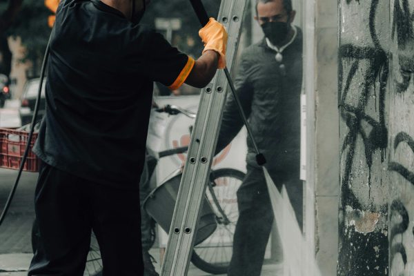 Professional worker using power washing equipment to clean graffiti from a building wall as part of post-construction cleaning.