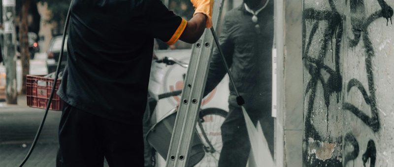 Professional worker using power washing equipment to clean graffiti from a building wall as part of post-construction cleaning.