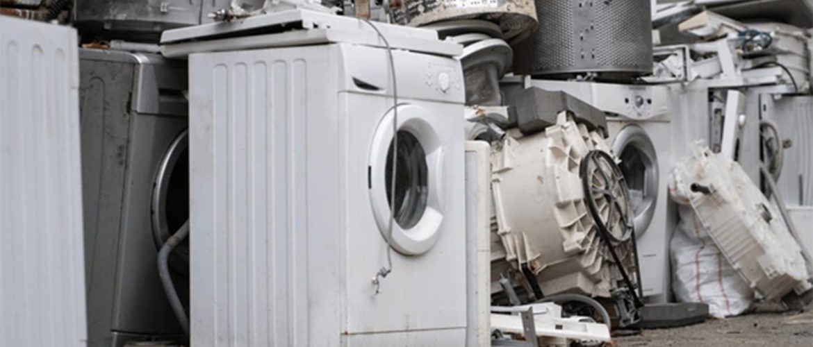 A pile of discarded washing machines and appliance parts, showcasing broken and worn-out equipment stacked outdoors.